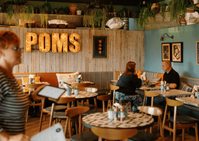 Interior of Poms Barton Marina, Burton-on-Trent, featuring rustic oak-top tables, upholstered café chairs, and fixed seating benches, creating a stylish and inviting waterfront café atmosphere.