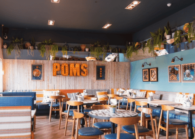 Interior of a waterfront café featuring rustic oak-top tables, upholstered café chairs, and fixed seating benches, creating a stylish and inviting waterfront café atmosphere.