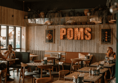 Interior of a waterfront café featuring rustic oak-top tables, upholstered café chairs, and fixed seating benches, creating a stylish and inviting waterfront café atmosphere.