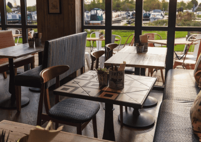Interior of a waterfront café featuring rustic oak-top tables, upholstered café chairs, and fixed seating benches, creating a stylish and inviting waterfront café atmosphere.