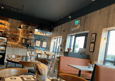 Interior of a waterfront café featuring rustic oak-top tables, upholstered café chairs, and fixed seating benches, creating a stylish and inviting waterfront café atmosphere.